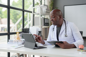 African American male doctor working in clinic at desk using laptop in medical coat and stethoscope. organ specialist The patient's anatomy, treatment methods, medical treatments.