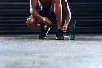 Fototapeta premium Healthy man, workout and ready with shoe laces for sports, exercise or fitness training in gym. African, male athlete and water bottle for cardio routine, safety or strong muscle for challenge