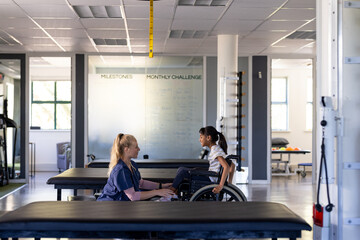 Assisting girl with cerebral palsy in wheelchair, therapist during rehabilitation session in clinic