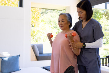 Female physical therapist assisting senior woman with dumbbell exercises at home