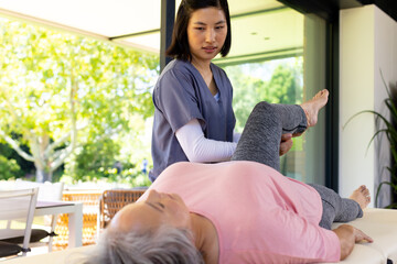 Female physiotherapist assisting senior woman with leg exercises at home