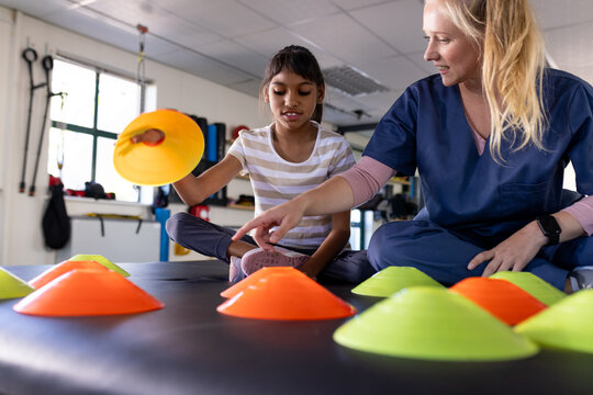 Female therapist assisting girl with cerebral palsy with rehabilitation exercises using cones