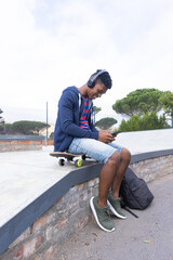 Listening to music with headphones, African American teenage boy skateboarding using smartphone, cop