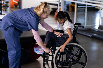Female therapist assisting girl with cerebral palsy in wheelchair, rehabilitation therapy session