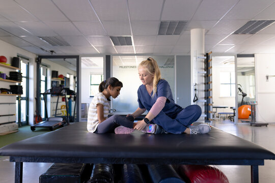 Assisting girl with cerebral palsy with leg exercises, female therapist in scrubs in rehabilitation 