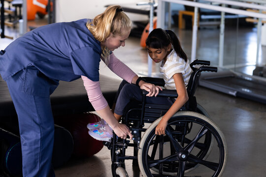 Female therapist assisting girl with cerebral palsy in wheelchair, rehabilitation therapy session