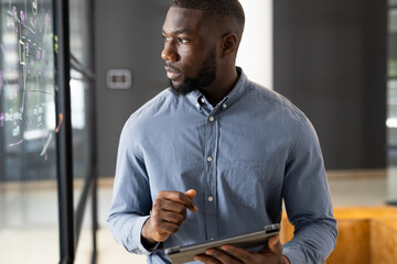 African American male business professional using tablet and writing on glass board