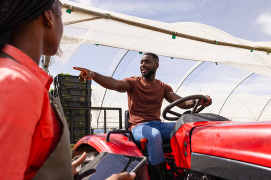 Farmer on tractor giving instructions to female worker with tablet in greenhouse