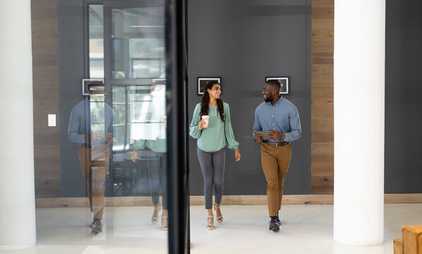 Walking in office, diverse business colleagues discussing work, holding coffee cup