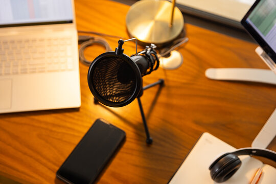 Podcasting setup with microphone, laptop, and smartphone on wooden desk, copy space