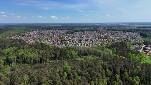Panoramic drone shot of a small rural village in Lithuania surrounded by deep forest under clear blue sky