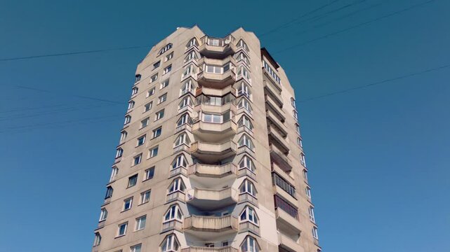 Footage captures the ascent on a high-rise residential concrete Soviet-era apartment tower block against a blue sky, showcasing its utilitarian design and historical architecture. Filmed in Latvia