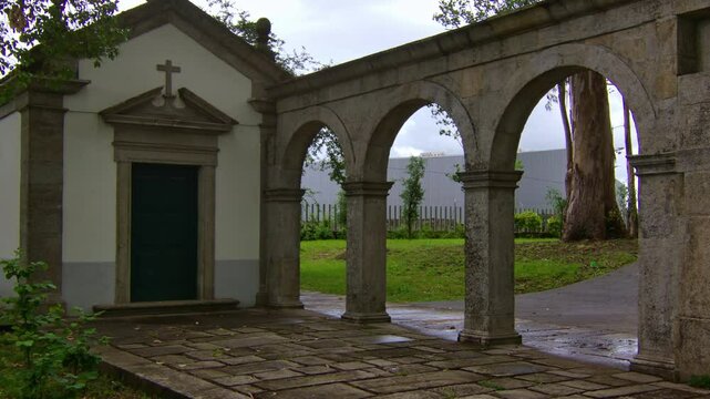 Static shot of a little christian chapel in a park with some stone arches by, in Porto.