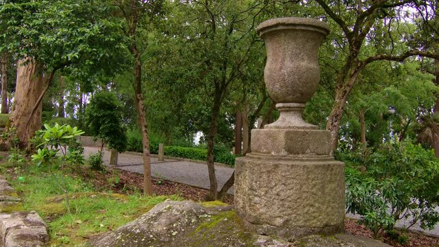 Static shot of a large stone jar in a park.