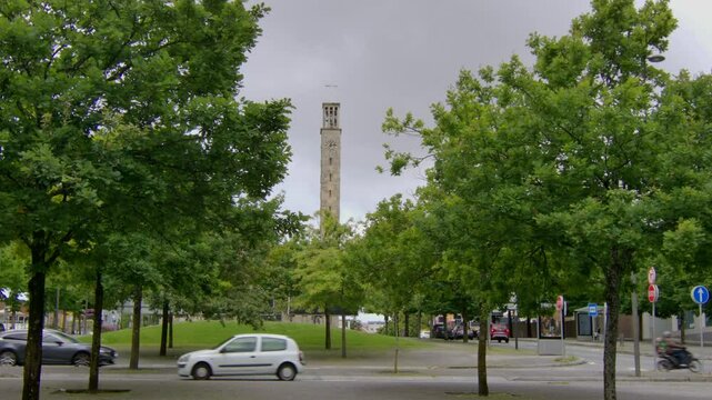 A tower in a park sticking up and cars driving around.