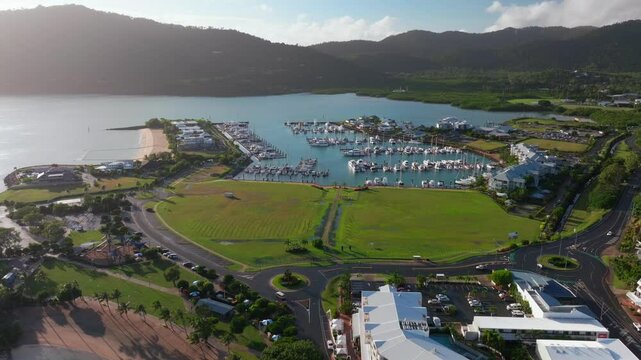 Port of Airlie Beach Bay Lagoon heart of Great Barrier Reef Whitsundays Whitehaven aerial drone green grass field sunny Coral Sea marina jetty Boathaven Beach sailboats cars forward reveal motion