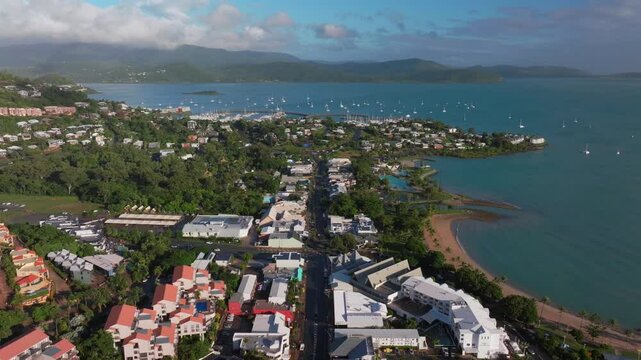 Airlie Beach Bay Lagoon heart of Great Barrier Reef Whitsundays Whitehaven aerial drone main street cars buildings sunrise morning mist sunny Coral Sea marina jetty sailboats  backwards motion