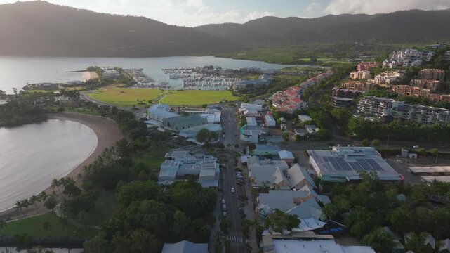 Airlie Beach Bay Lagoon heart of Great Barrier Reef Whitsundays Whitehaven aerial drone sun clouds main street cars buildings mist sunny Coral Sea marina jetty sailboats forward reveal motion