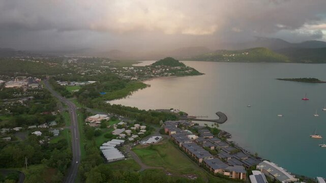 Port Airlie Beach Bay Lagoon Coral Sea marina aerial drone road cars towards Cannonvale sunrise morning rain shower heart of Great Barrier Reef Whitsundays Whitehaven jetty yachts forward motion