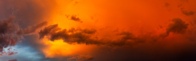 Panoramafoto einer abziehenden Gewitterwolke, die vom Licht der untergehenden Sonne orange...