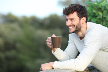 Happy man in a terrace drinking coffee looking away