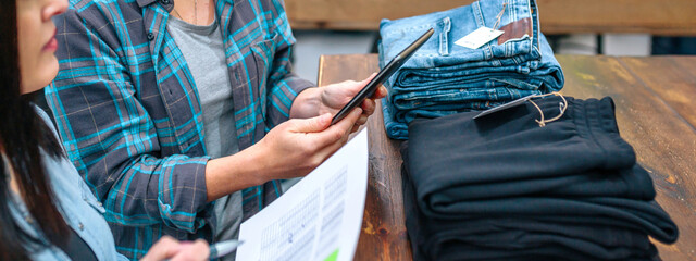 Banner of unrecognizable woman holding digital tablet next to partner while checking clothes stock on store. Female entrepreneurs looking apparel inventory in clothing shop. Small business concept.