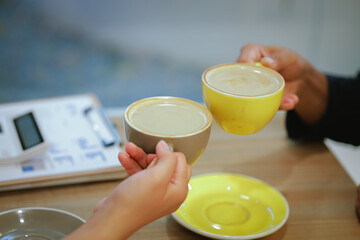 Close-up of a man and woman clinking white coffee cups in a coffee shop. While talking about business matters
