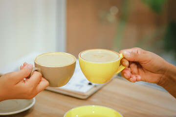 Close-up of a man and woman clinking white coffee cups in a coffee shop. While talking about business matters