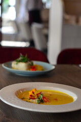 yellow vegetable soup with herbs, squid, pumpkin soup, herbs, plate, serving restaurant table, lunch menu 