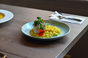 The plate features perfectly roasted cod with crispy skin, served on a vibrant Italian saffron risotto.