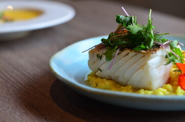 The plate features perfectly roasted cod with crispy skin, served on a vibrant Italian saffron risotto.