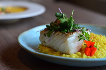 The plate features perfectly roasted cod with crispy skin, served on a vibrant Italian saffron risotto.
