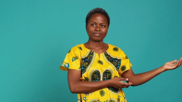 Confident smiling girl indicating direction to left or right sides in studio, pointing her index fingers around. Young natural person wears traditional african attire with tribal native elements