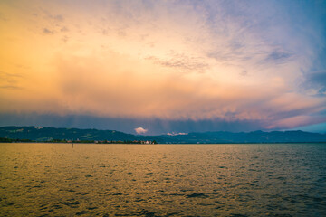 Germany, Lindau island village houses, bodensee lake water panorama, view to mountains, alps, nature landscape after sunset on stormy day with magical red sky