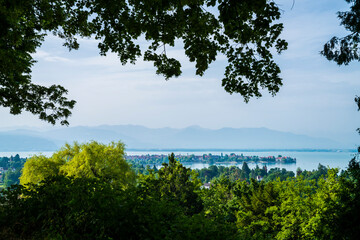 Germany, Lindau old town houses on island surrounded by silent bodensee lake water early morning, alps mountains in foggy atmosphere, panorama view