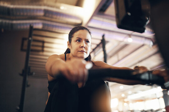 Fit and focused young woman in sportswear doing a rowing machine exercise during a workout session alone at the gym