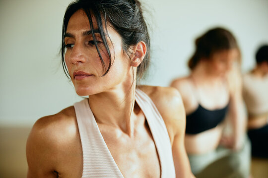 A concentrated woman immerses herself in yoga, together with her friends. They sweat as they stretch