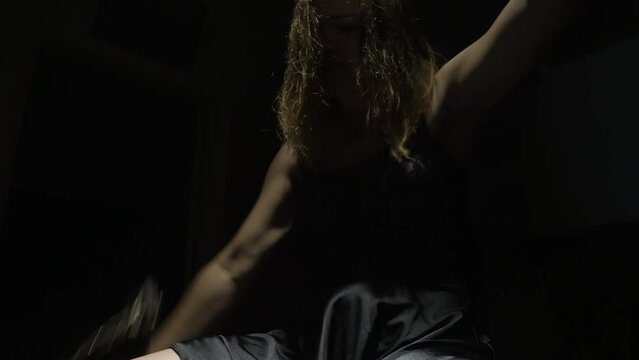 A woman with long hair is shackled in chains with a lock hanging from them. She struggles to free herself and eventually succeeds