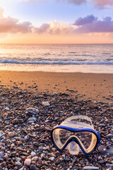 ocean cloudy morning landscape with diving mask on sea coast on foreground, sand of a beach, blue sea with surf and waves and cloudy sunset or sunrise on background