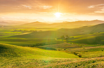 Fototapeta premium spring season green landscape of green field and meadow in a hill countryside with mountains and beautiful sunset sky on background