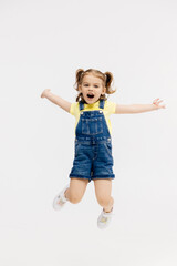 Little girl dancing in the studio on a white background. Happy energetic girl having fun and enjoying her childhood. Concept of fashion, style and happy children's emotions.