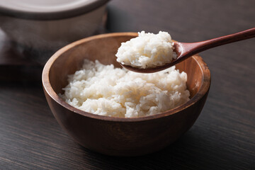 나무그릇에 있는 흰 쌀밥을 숟가락으로 뜨고 있다.