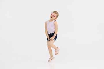 Little girl dancing in the studio on a white background. Happy energetic girl having fun and enjoying her childhood. Concept of fashion, style and happy children's emotions.