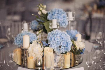 Flowers and candles on table. blue and white flowers decorate the table. Beautiful table set with candles and flowers for a festive event, party or wedding reception. 