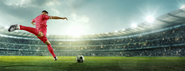 Banner. Cinematic view. Soccer player in red strikes ball with power, aiming for goal in brightly lit stadium filled with spectators. Concept of sports games, competition, championship, tournament. Ad