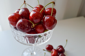 A crystal glass bowl is filled with fresh, ripe cherries, their vibrant red color and glossy surface looking incredibly appetizing. A few cherries rest nearby on the table, emphasizing their natural b