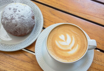 A cup of cappuccino and a plate with a bun are on the table