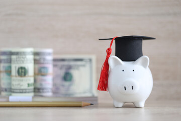 Graduation hat on piggy and banknotes on wooden background, Saving money for education concept