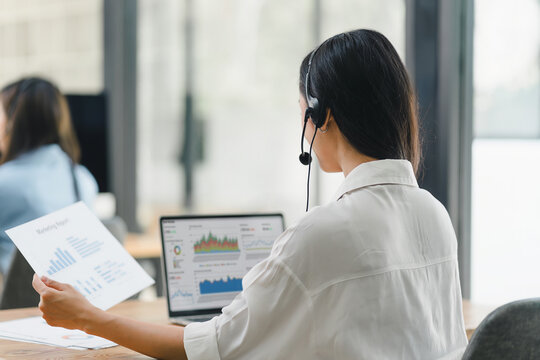 Operator wearing a headset, using a dashboard on laptop for data analysis in modern office. Soft focus