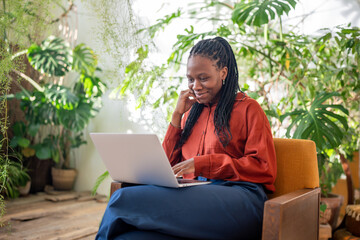 Relaxed african american woman freelancer with laptop on knees smiling glad working result sitting...